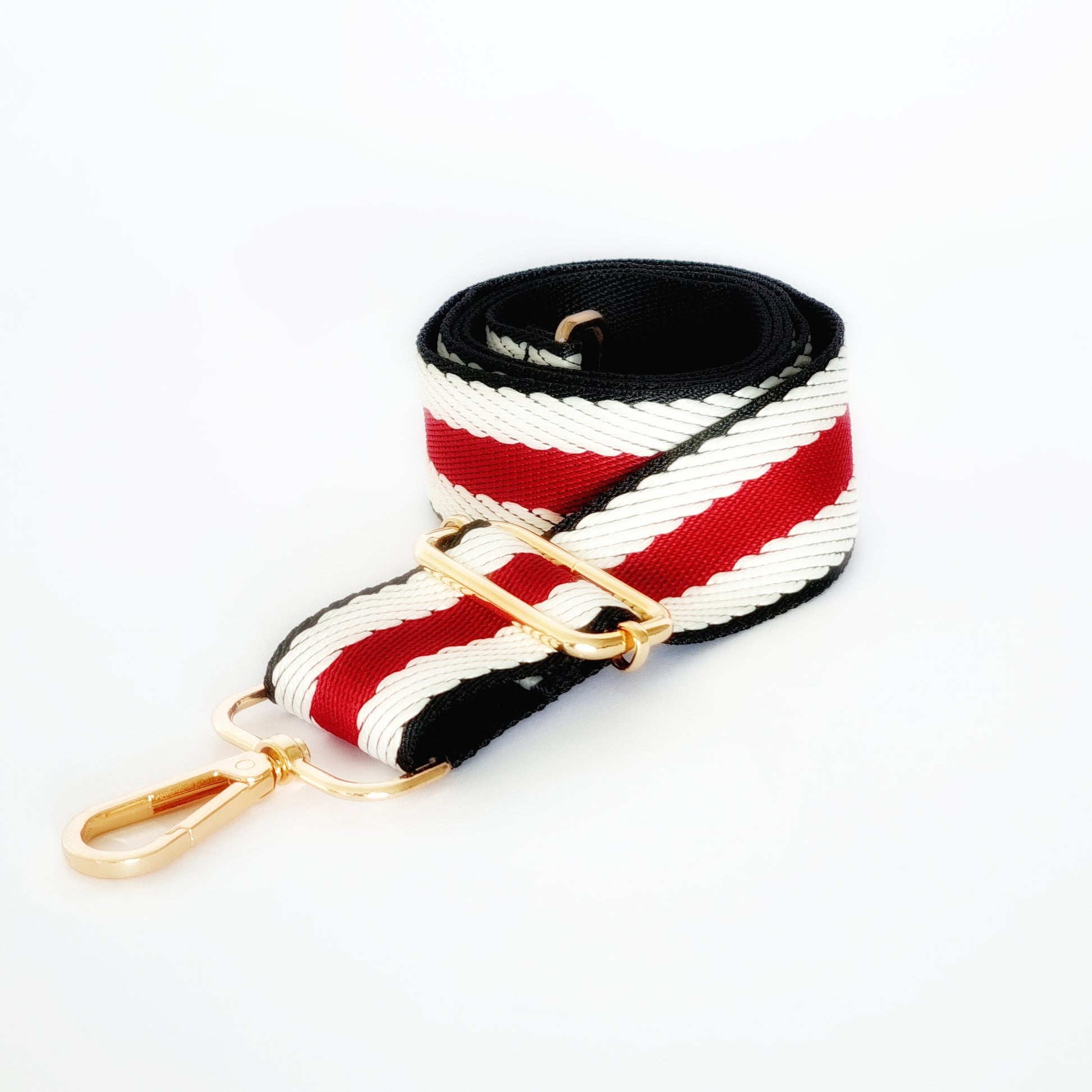 A woven fabric strap with a red and black color block pattern, featuring  gold hardware 