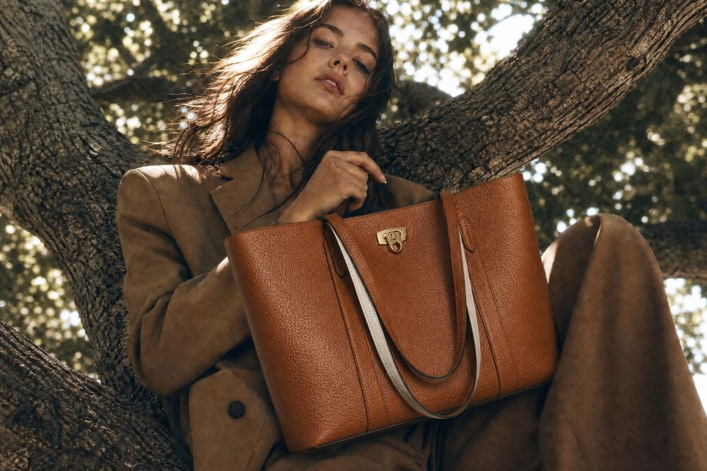 Woman holding a brown leather  tote handbag under a tree
