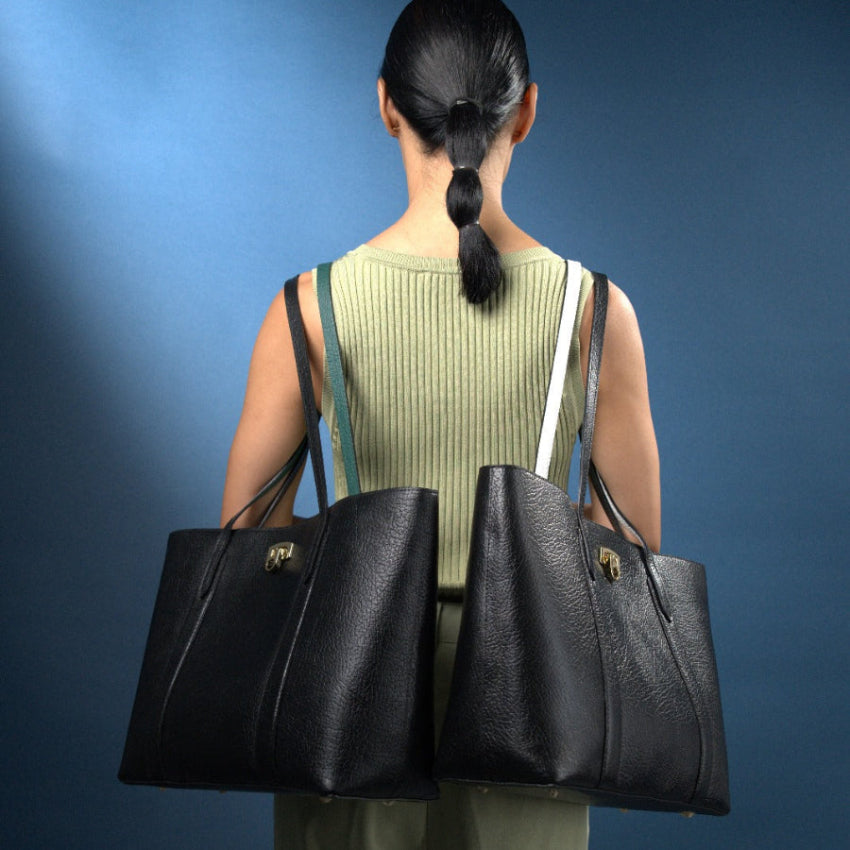 Model holding two black tote handbags against a blue background